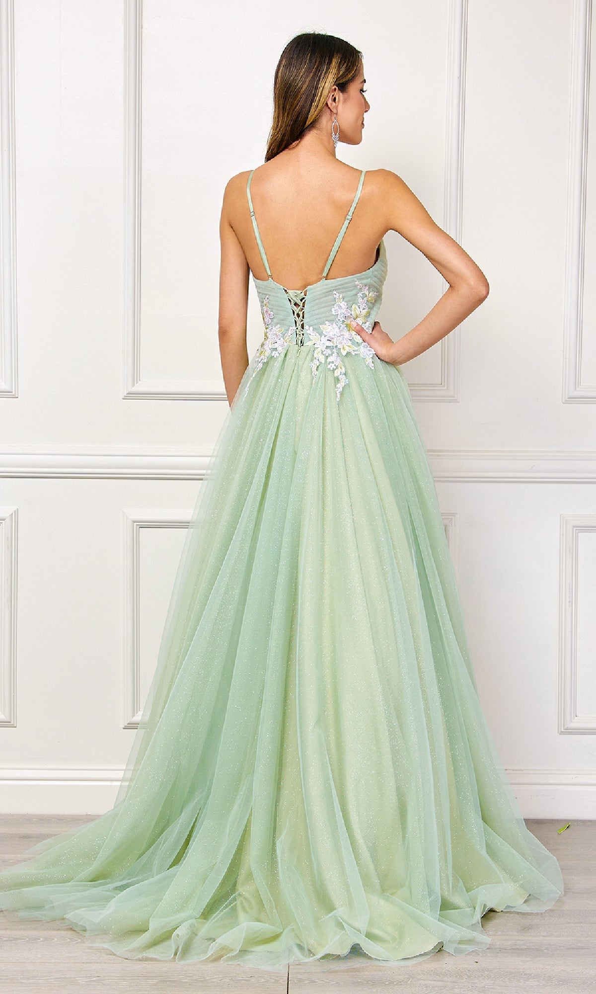 A woman faces away, wearing the Amelia Couture SU088 long pastel prom ball gown with thin straps, a lace-up back, and delicate floral embroidery at the waist.